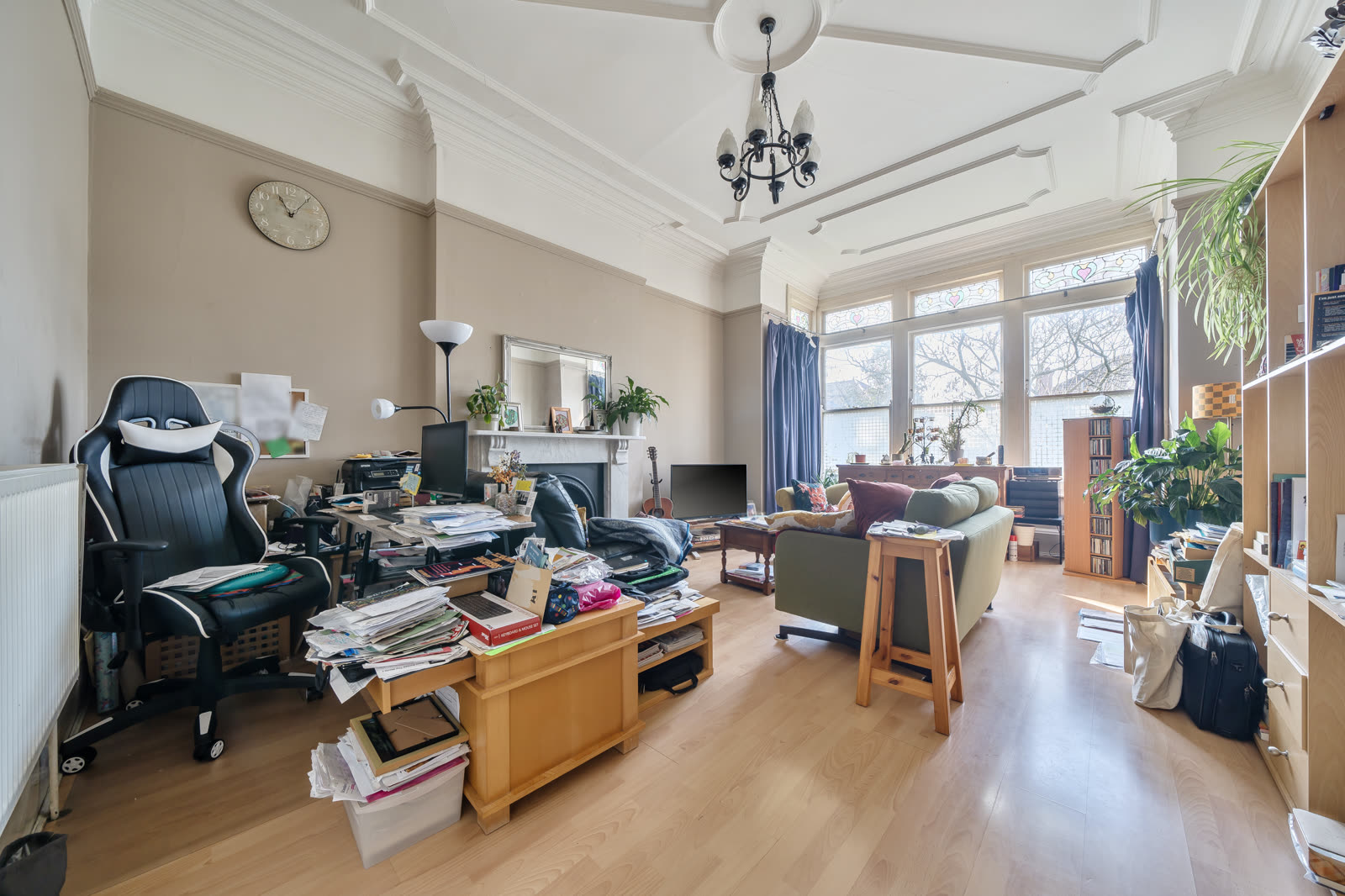 Living room as photographed in occupied state, cluttered with desk, gaming chair, papers and lifestyle clutter