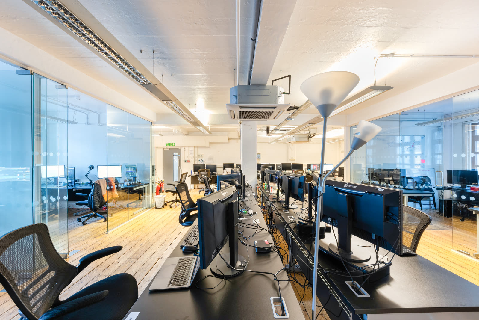 Commercial office, long shot with glass partitioned meeting rooms on either side, monitors and cables on the desks, as photographed